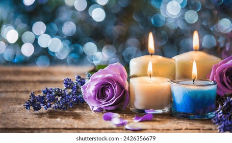 Colorful dreamy candles on bokeh background on wooden table surrounded with pink flowers. Dreamy design, Candles against bokeh lights background for clean Spa, valentine, wedding theme. Love and Peace