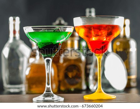 Colorful drink on the background of bottles in original shapes, cocktail drink with ice cubes, party night