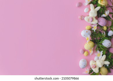 Colorful Easter Chocolate Eggs, Bunnies And Spring Flowers Border Flat Lay On Pink Background. Happy Easter! Stylish Easter Layout. Greeting Card Or Banner Template
