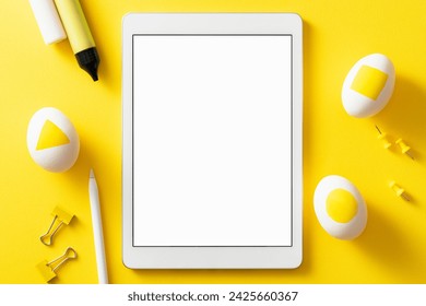Colorful easter concept. Blank screen digital tablet with clipping path. Easter eggs,pushpins, binder clips and color pens on yellow background.
