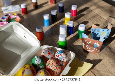 Colorful Easter Egg Decorating with Art Supplies.
Get ready for Easter with this charming scene of egg decorating. Hand-painted eggs, colorful paints, and paper craft chickens are spread out on a wooden table, capturing the essence of holiday creativity.