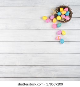 Colorful Easter Egg Nest Overflowing From Up Above With Extra White Or Gray Wood Board Background For Room Or Space For Copy, Text, Words.  A Flat Lay With Square Crop