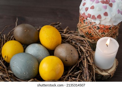 Colorful Easter Eggs In Birds Nest, Cake And Candle On A Wooden Table