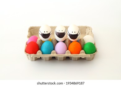  Colorful Easter eggs in egg carton on the table with copy space for text. Easter eggs with Corona virus COVID19 protection concepts. DIY Do It Yourself easter eggs wearing mask for Easter holidays