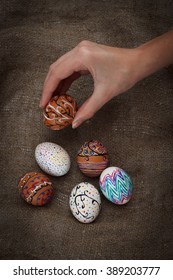 Colorful Easter Eggs On Burlap, Female Hand Chose And Pick One, Top View Close Up