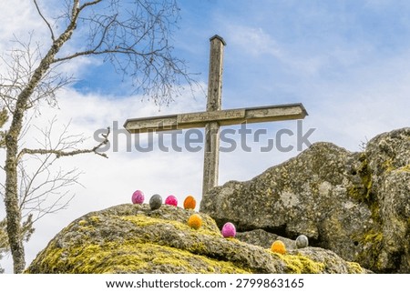 Colorful Easter eggs placed on moss-covered rocks beneath the summit cross of Hoher Sachsen mountain near Grafenau in the Bavarian Forest, Germany. Seasonal spring scene photographed outdoors in natural daylight.