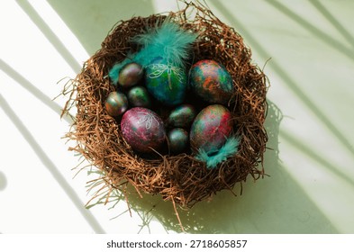 Colorful Easter eggs rest in a rustic nest adorned with decorative feathers. Sunlight casts gentle shadows enhancing the vibrant hues and intricate designs.