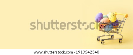 Colorful easter eggs in shopping cart on yellow background. Copy space.