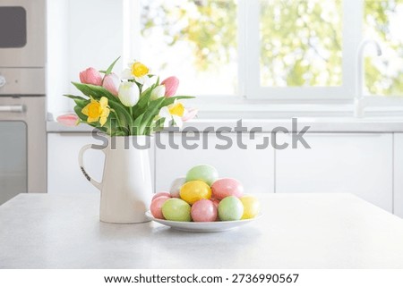 Colorful Easter eggs and spring flowers on white table on modern kitchen interior background