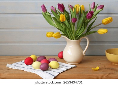 Colorful easter eggs and tulips create a festive centerpiece on a rustic wooden table