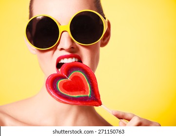 Colorful edgy fashion portrait of woman with heart shaped lollipop. 