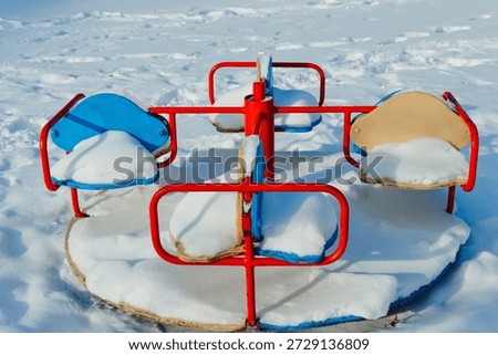 Colorful empty carousel covered with snow in winter playground. Cold season, childhood memories, outdoor recreation, concept of loneliness and frozen time. Perfect for seasonal or emotional designs.