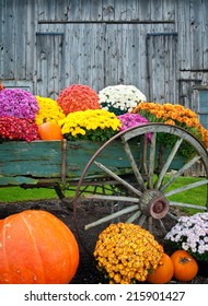 Colorful Fall Flowers And Pumpkins In Old Antique Wagon Against A Barn Background Vertical.