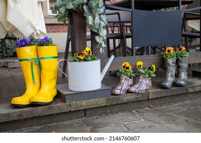 Colorful Family Rain Boots With Pansy Flowers On A Rainy Day Outdoors, Horizontal,