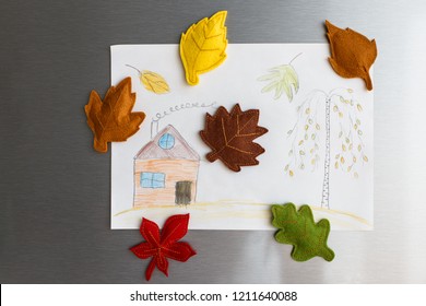 Colorful Felt Autumn Leaves On Refrigerator Door. Children Picture With House And Tree Hanging On Fridge Door. White Kitchen On Background. Diy Fall Autumn Decoration For Home