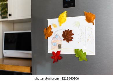 Colorful Felt Autumn Leaves On Refrigerator Door. Children Picture With House And Tree Hanging On Fridge Door. White Kitchen On Background. Diy Fall Autumn Decoration For Home