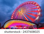 Colorful Ferris wheel at a funfair in Germany with motion blur. Glowing red, yellow lines and circles from long exposure light trails. Popular twilight ride at blue hour. Roundabout or merry-go-round.