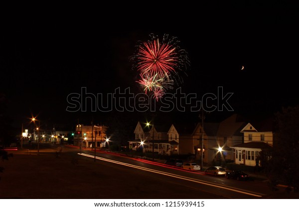 colorful\
fireworks bursting over a nighttime small town with car headlights\
and taillights streaming down the\
street