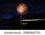 Colorful fireworks illuminate the night sky near a tranquil lake, creating a dazzling display of lights