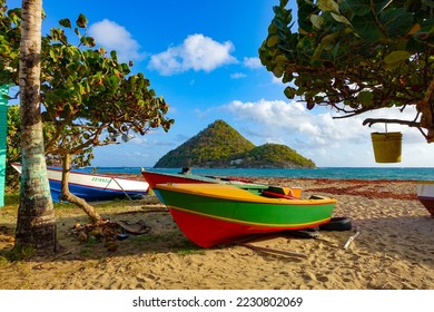 Colorful fishing boat sits on a sandy beach between trees with a tropical island in the distance - Powered by Shutterstock