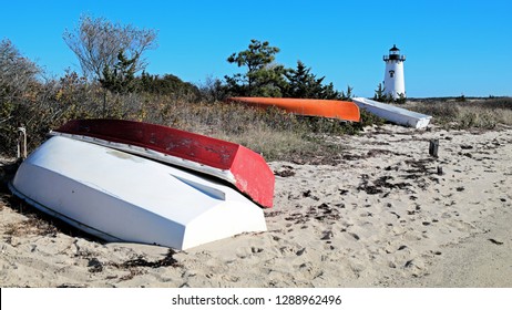Colorful Fishing Boats Line The Shore With A White New England Lighthouse In The Distance