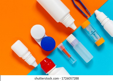 Colorful flat lay of vision correction lenses equipment on blue and orange background : eye drops, containers, lenses, twizzlers, liquids