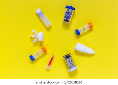 Colorful flat lay of vision correction lenses equipment on yellow background : eye drops, containers, lenses, twizzlers, liquids