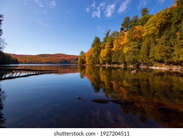 Colorful forest full of bright fall foliage reflecting on calm water in Gatineau Park, Quebec, Canada