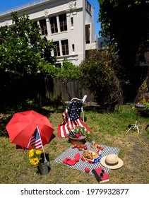 Colorful Fourth Of July Backyard Picnic With Flags, Basket, And Food With A Black And White Checkered Cloth Spread On The Grassy Ground. 