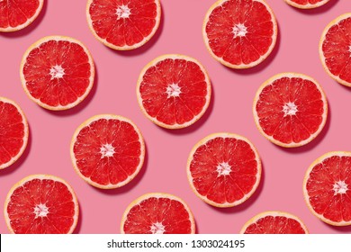 Colorful fruit pattern of fresh grapefruit slices on pink background. Minimal flat lay concept.