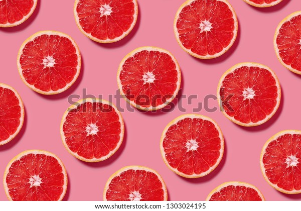 Colorful fruit pattern of fresh\
grapefruit slices on pink background. Minimal flat lay\
concept.