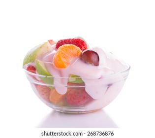 Colorful fruit salad in a glass bowl, topped with pink strawberry yogurt, on light background