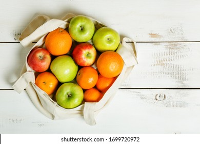 Colorful fruits (apples, oranges, tangerines) in a reusable eco bag on a white background. Healthy food, vitamins. Top view.