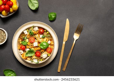 Colorful full grain fusilli pasta warm salad with feta cheese, cherry tomatoes, herbs, green pea and basil leaves on black stone background top view, copy space for your design. - Powered by Shutterstock