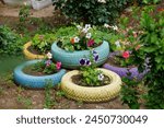 A colorful garden with a variety of flowers and plants in different sized planters made from old tires