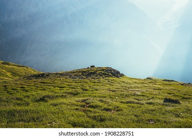 Colorful green landscape with rocks and hills on background of giant mountain wall in sunlight. Minimalist vivid sunny scenery with sun beams and solar flare. Minimal alpine view. Scenic minimalism. - Powered by Shutterstock