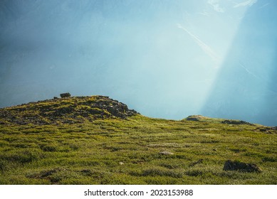 Colorful green landscape with rocks and hills on background of giant mountain wall in sunlight. Minimalist vivid sunny scenery with sun beams and solar flare. Minimal alpine view. Scenic minimalism. - Shutterstock ID 2023153988