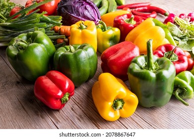 Colorful green , red and yellow peppers paprika  and other vegetables on a wooden table 
