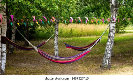 Colorful hammocks hanging outside in a park between trees with some flags above them - Powered by Shutterstock