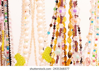 Colorful handmade chains of beads, pearls and natural stones in front of beige background.