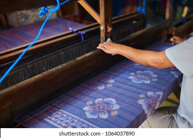 Colorful handmade sarong or saree made of cotton and silk. Ethnic clothing of Indonesian woman. Weaving and manufacturing of handmade fabric. Women's hands make cloth on the loom. Selective focus.