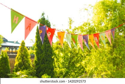 Colorful Happy Birthday Bunting Garland (banner) Hanging Outdoor - Garden Party Decoration. Sunny Summer Or Spring Day, Greenery As Background.