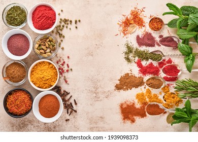 Colorful herbs and spices for cooking: turmeric, dill, paprika, cinnamon, saffron, basil and rosemary. Indian spices. On light brown stone background. Top view.