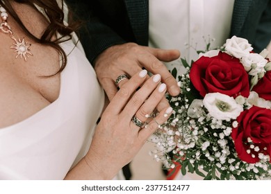 A colorful horizontal wedding photograph featuring a close-up of the bride and groom's hands adorned with wedding rings, set against a background close-up of the bride and groom, along with the bridal