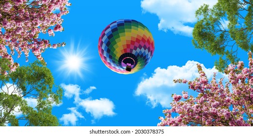 Colorful Hot Air Balloon In The Blue Sky. Green Tree Branches And Pink Spring Flowers. Bottom View Stretch Ceiling Sky Picture.