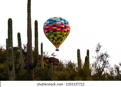 Colorful hot air balloon flying over saguaro national park. A hill covered in cactus, green plants and rocks. Beautiful Sonoran Desert landscape in the Southwest. Pima County, Tucson, Arizona. 2019.