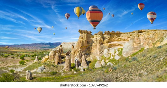 Colorful hot air balloons flyi in blue sky above unusual rocky landscape in Cappadocia near Goreme, Turkey