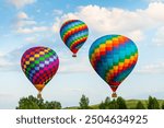 Colorful hot air balloons flying over the green hills and trees at sunset. Rainbow colored balloons in the blue sky. Beautiful summer landscape. 