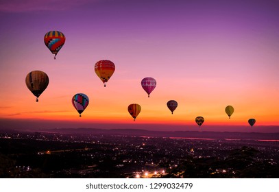 The Colorful hot air Balloons  flying above city on sunset time before dark coming with colorful of light and a beautiful twilight and sunset sky background.