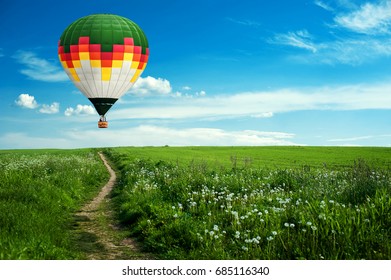 Colorful hot-air balloon flying over the field against blue cloudy sky